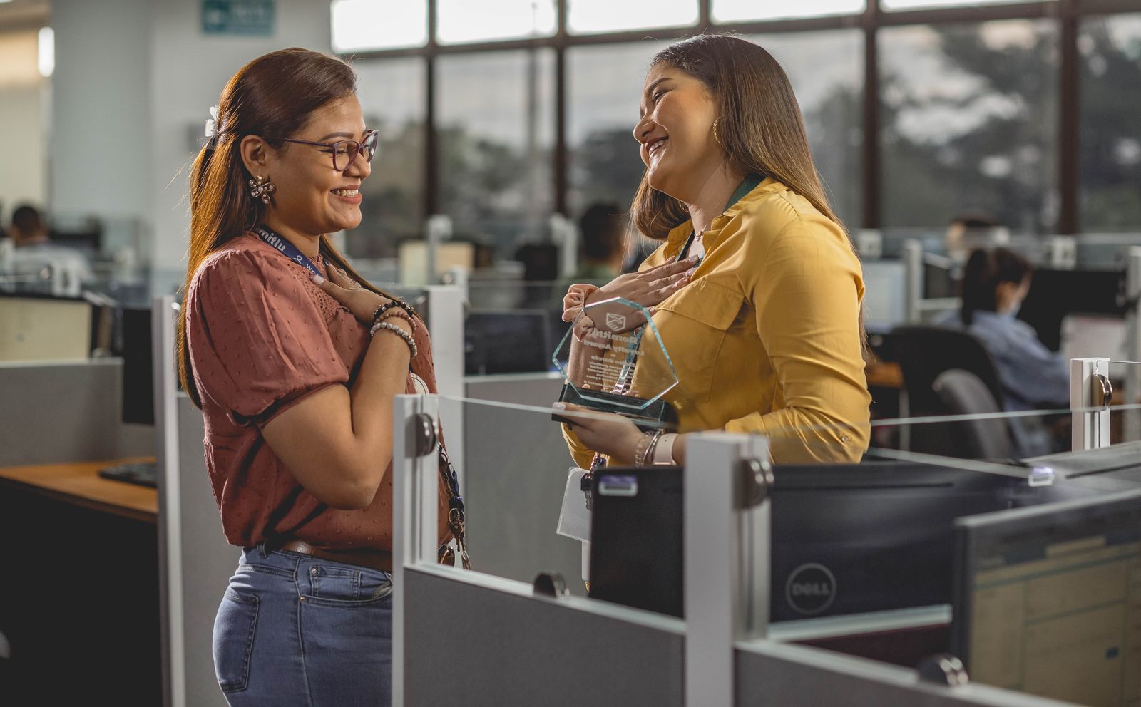 Two coworkers smiling and sharing a joyful moment while receiving an award in the office.