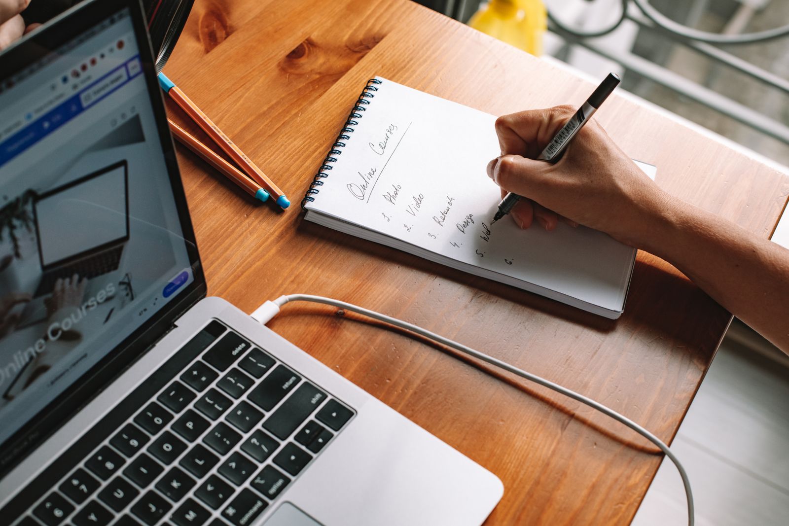 A person taking notes while researching online courses on a laptop.