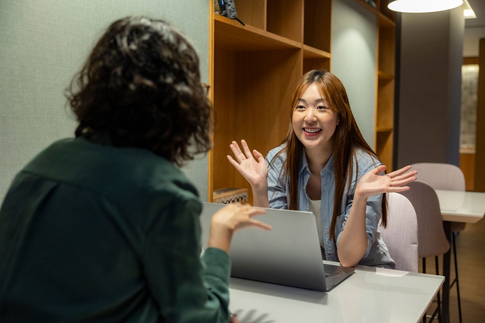 Two colleagues having a cheerful, ongoing conversation at their desk