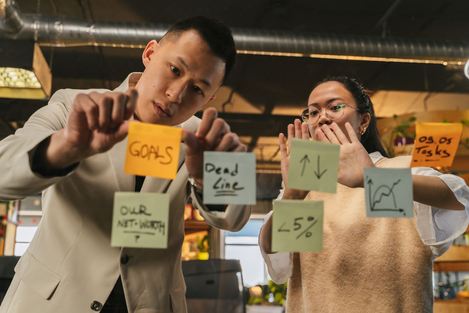 Two professionals organizing goals with sticky notes on a glass wall