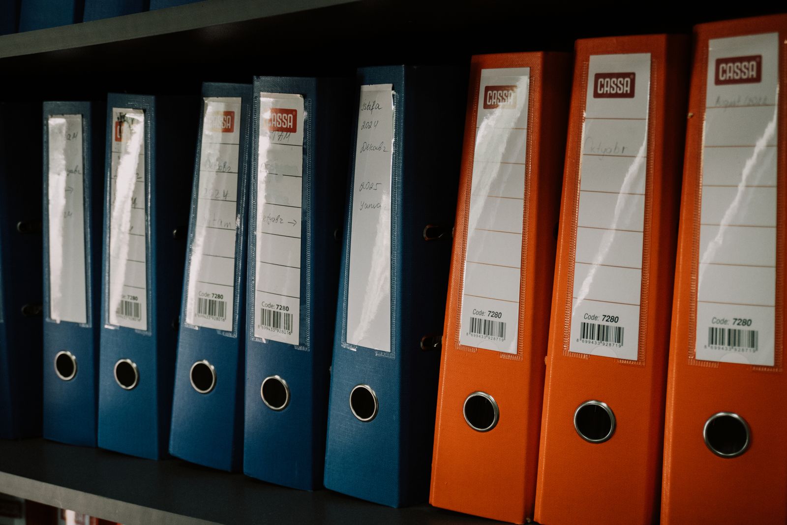 A row of colorful, labeled binders organized on an office shelf