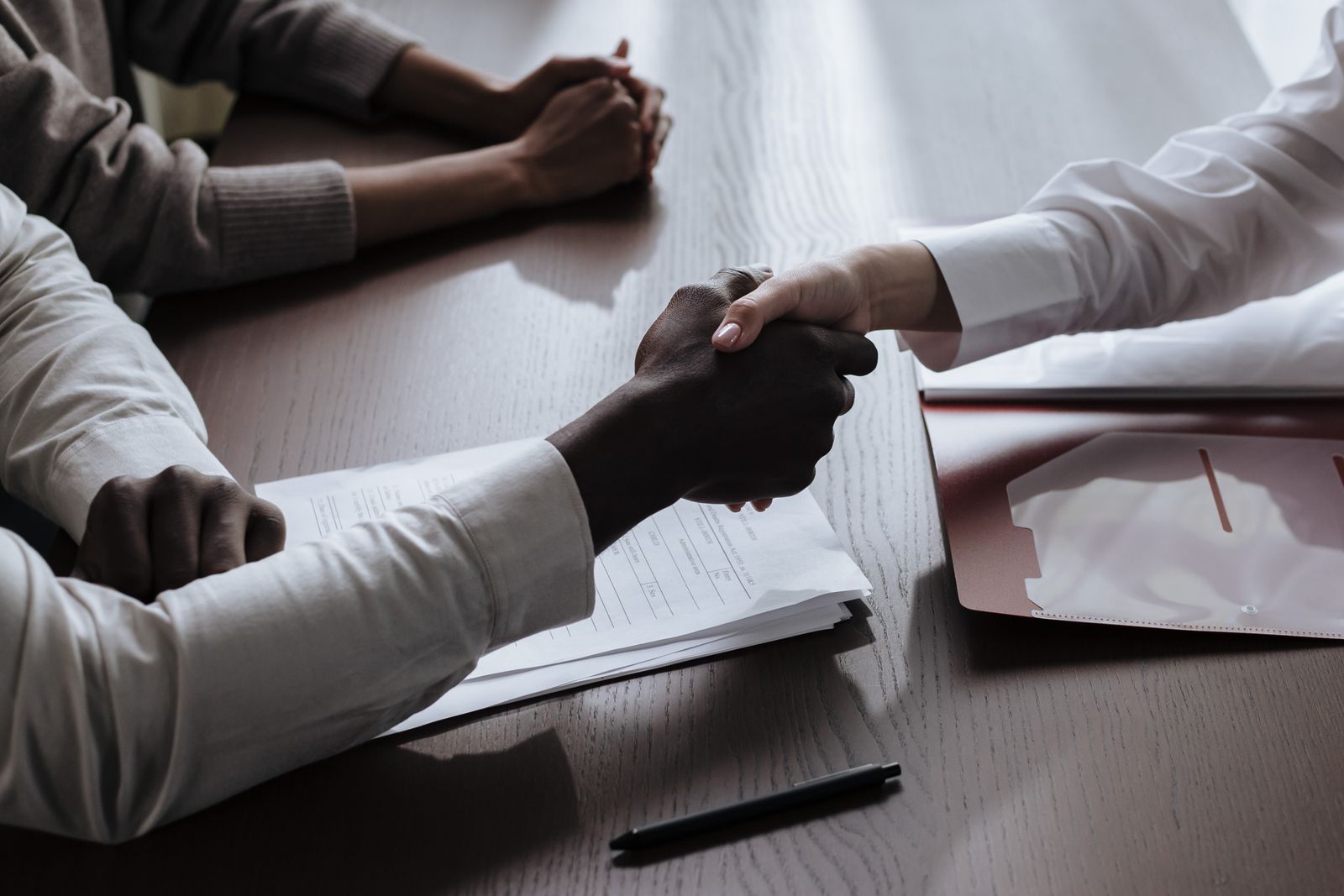 Two people shaking hands over a signed offer agreement