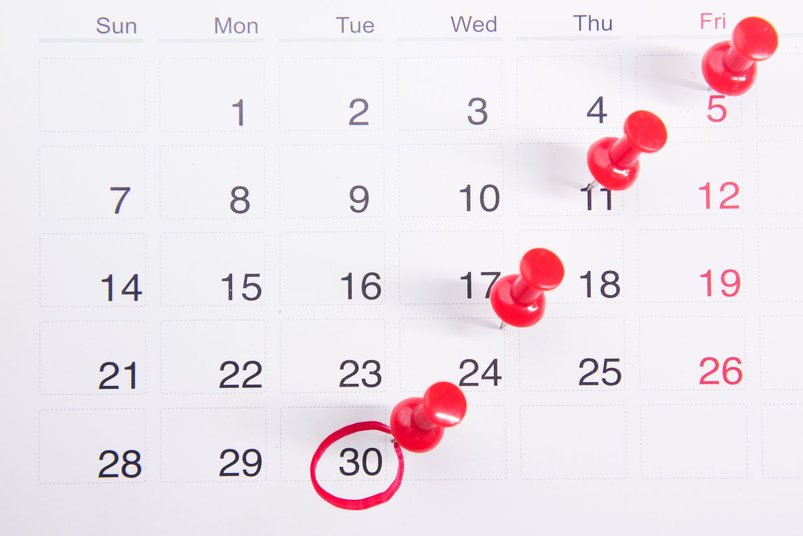 A close-up of a desk calendar with red push pins marking important dates.