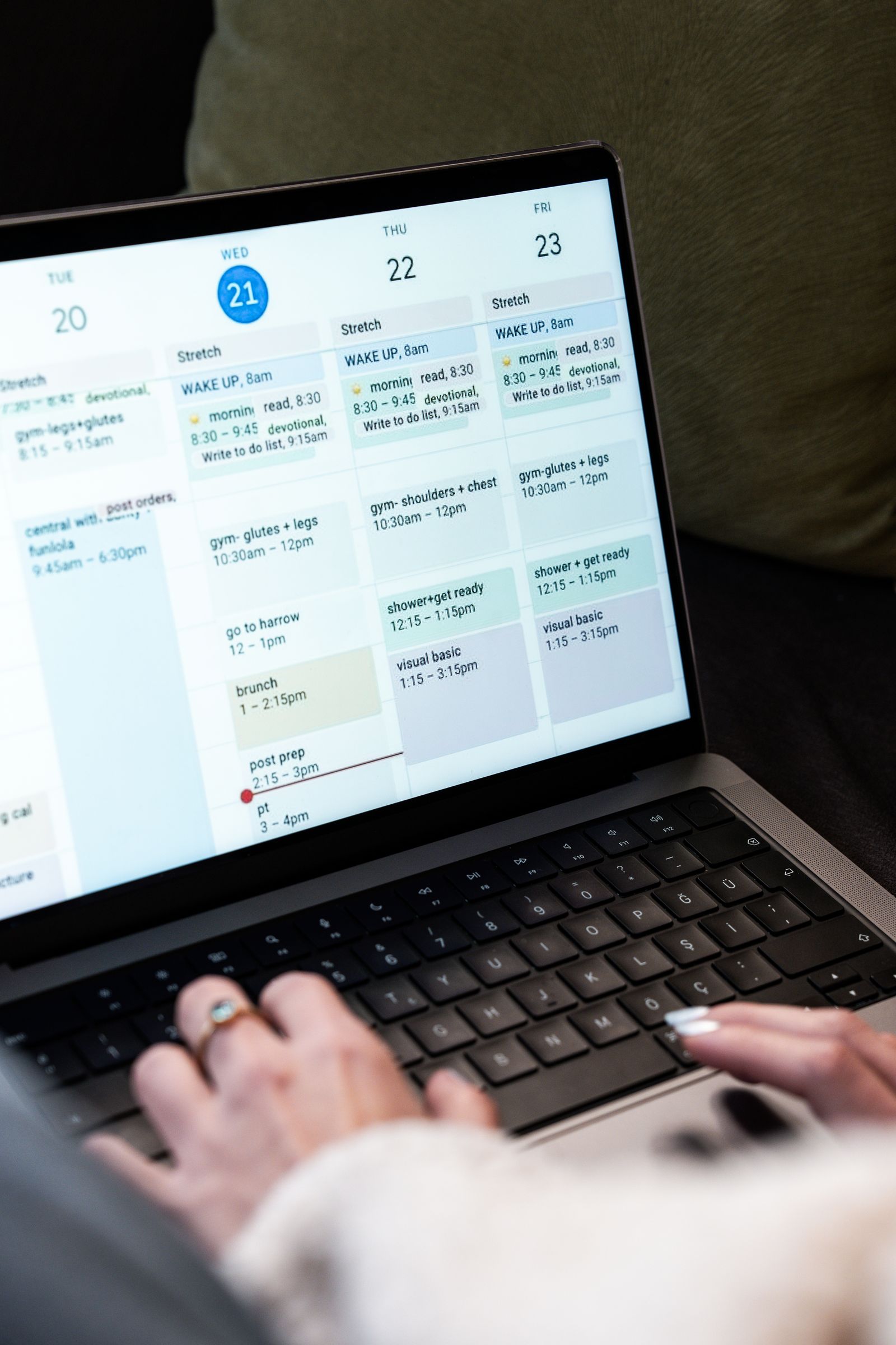 A woman typing on a laptop while planning her weekly work schedule on a digital calendar.